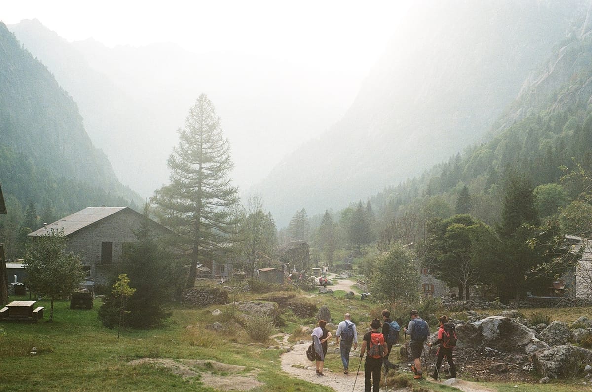 Hikers following a trail through a misty mountain valley beside a cabin.
